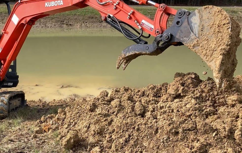Excavator removing accumulated soil beside the water